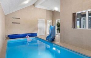 An indoor swimming pool with a slide, a blue lounge chair, and a potted plant. - Amazing home in Bogense with sauna (Bogense)