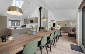 Une cuisine moderne avec une table à manger en bois, des chaises vertes, des luminaires suspendus et une vue sur l’extérieur.