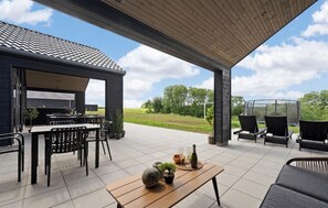 Une terrasse extérieure dotée d’un espace salon abrité, d’une table à manger et offrant une vue sur le paysage environnant.