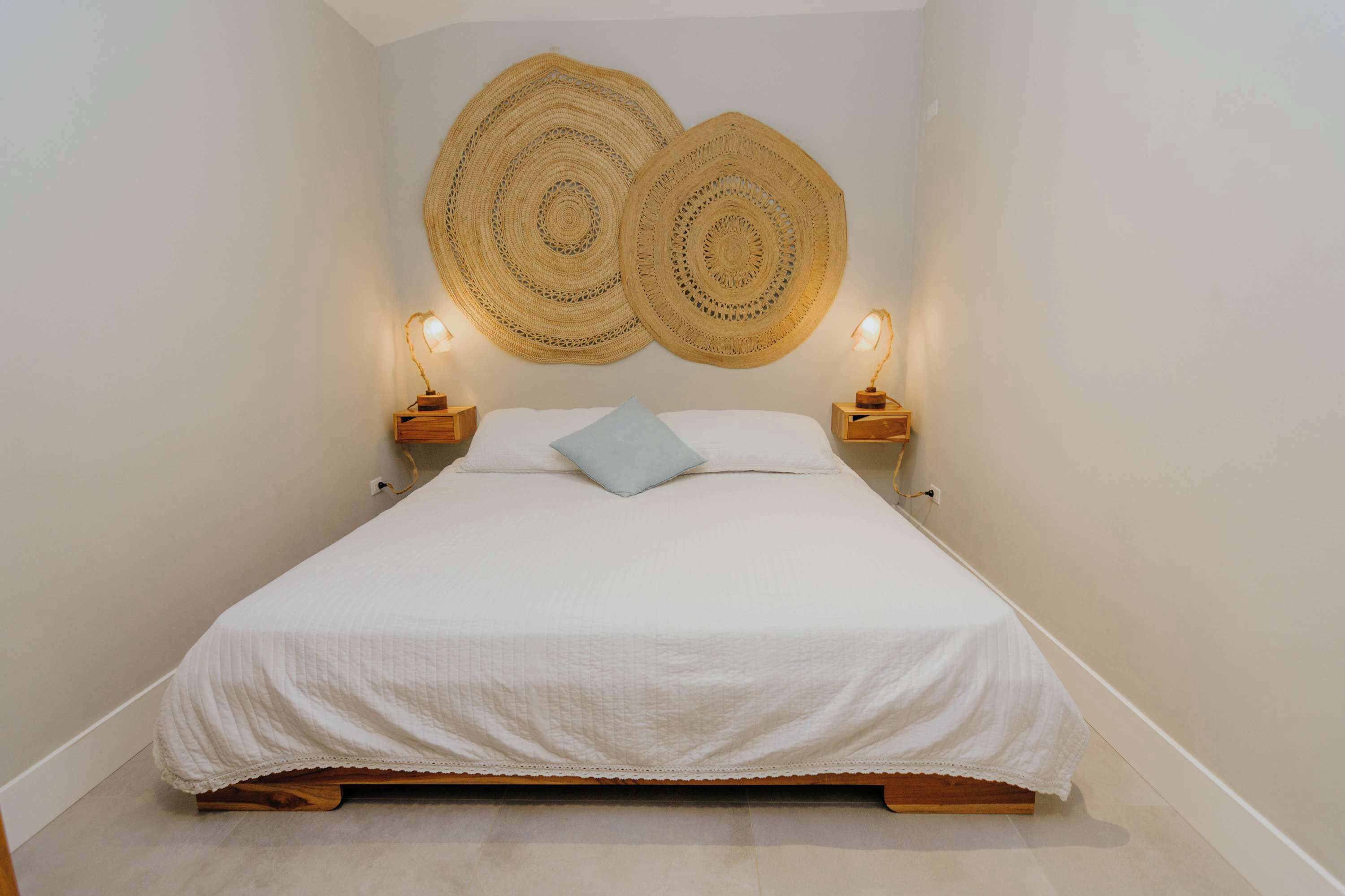 Ein Bett mit weißer Bettdecke, zwei an der Wand befestigte Webkunstwerke und zwei Nachttischlampen.