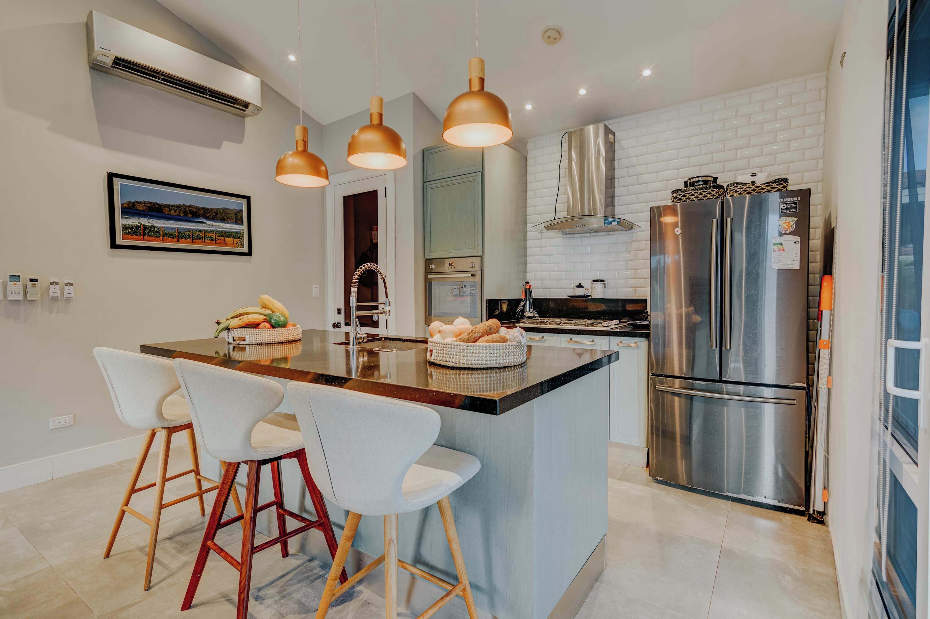 Une cuisine moderne dotée d’un îlot central, d’appareils électroménagers en acier inoxydable, de luminaires suspendus et d’un tableau encadré au mur.