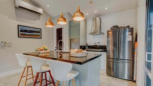 A modern kitchen with a central island, stainless steel appliances, pendant lighting, and a framed picture on the wall. - Family Surf Villa with Resort Amenities at Venao (Las Escobas del Venado)