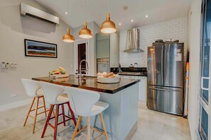 Una cocina moderna con una isla central, electrodomésticos de acero inoxidable, iluminación colgante y un cuadro en la pared.