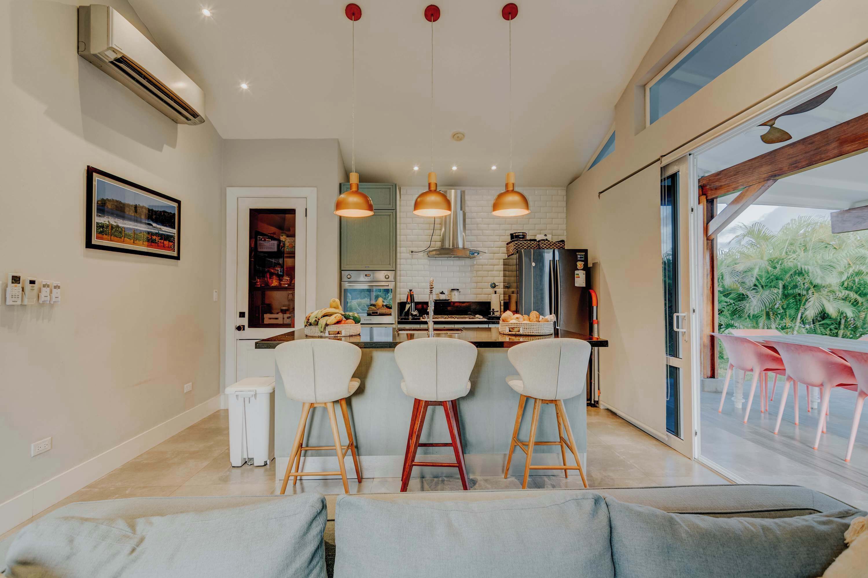 Une cuisine moderne dotée d’un îlot central, de luminaires suspendus et d’un coin repas avec des chaises roses.