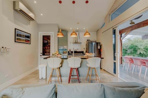 Uma cozinha moderna com uma ilha central, luminárias pendentes e um espaço de jantar com cadeiras cor-de-rosa.