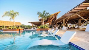 A pool area with lounge chairs, palm trees, and a thatched-roof structure. - Family Surf Villa with Resort Amenities at Venao (Las Escobas del Venado)