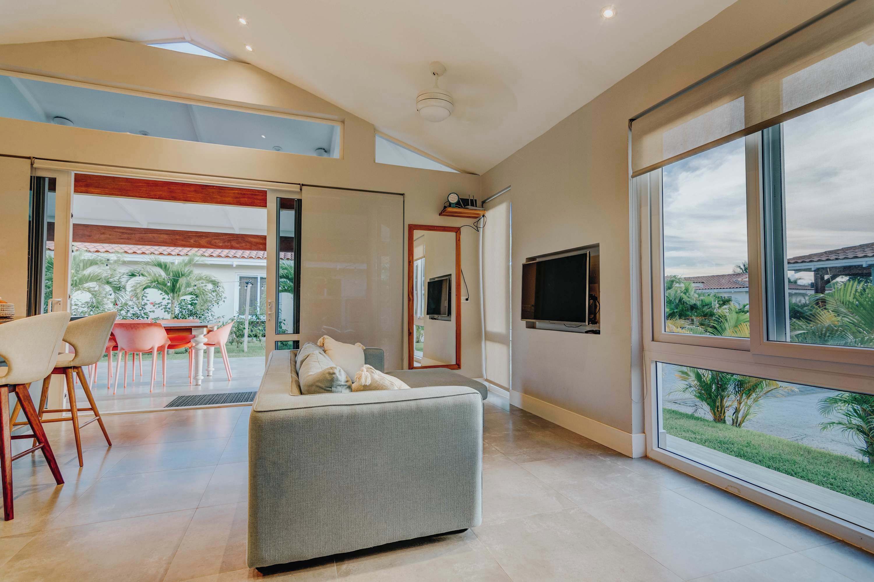 A modern living room with a sofa, dining area, and large windows offering a view of the outdoors.