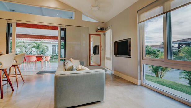 A modern living room with a sofa, dining area, and large windows offering a view of the outdoors. - Family Surf Villa with Resort Amenities at Venao (Las Escobas del Venado)