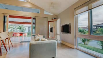 A modern living room with a sofa, dining area, and large windows offering a view of the outdoors.