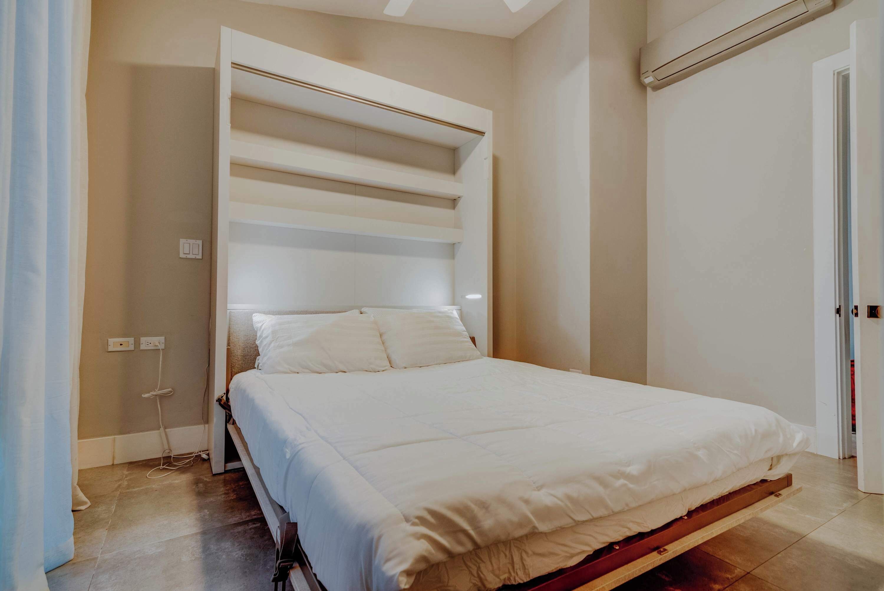 A bedroom with a bed, a built-in shelf unit, and a door.