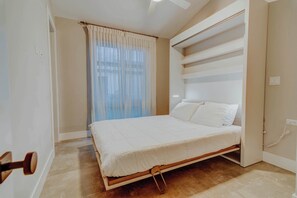 Ein Schlafzimmer mit Bett, einem Fenster mit Vorhängen und einer eingebauten Regaleinrichtung.