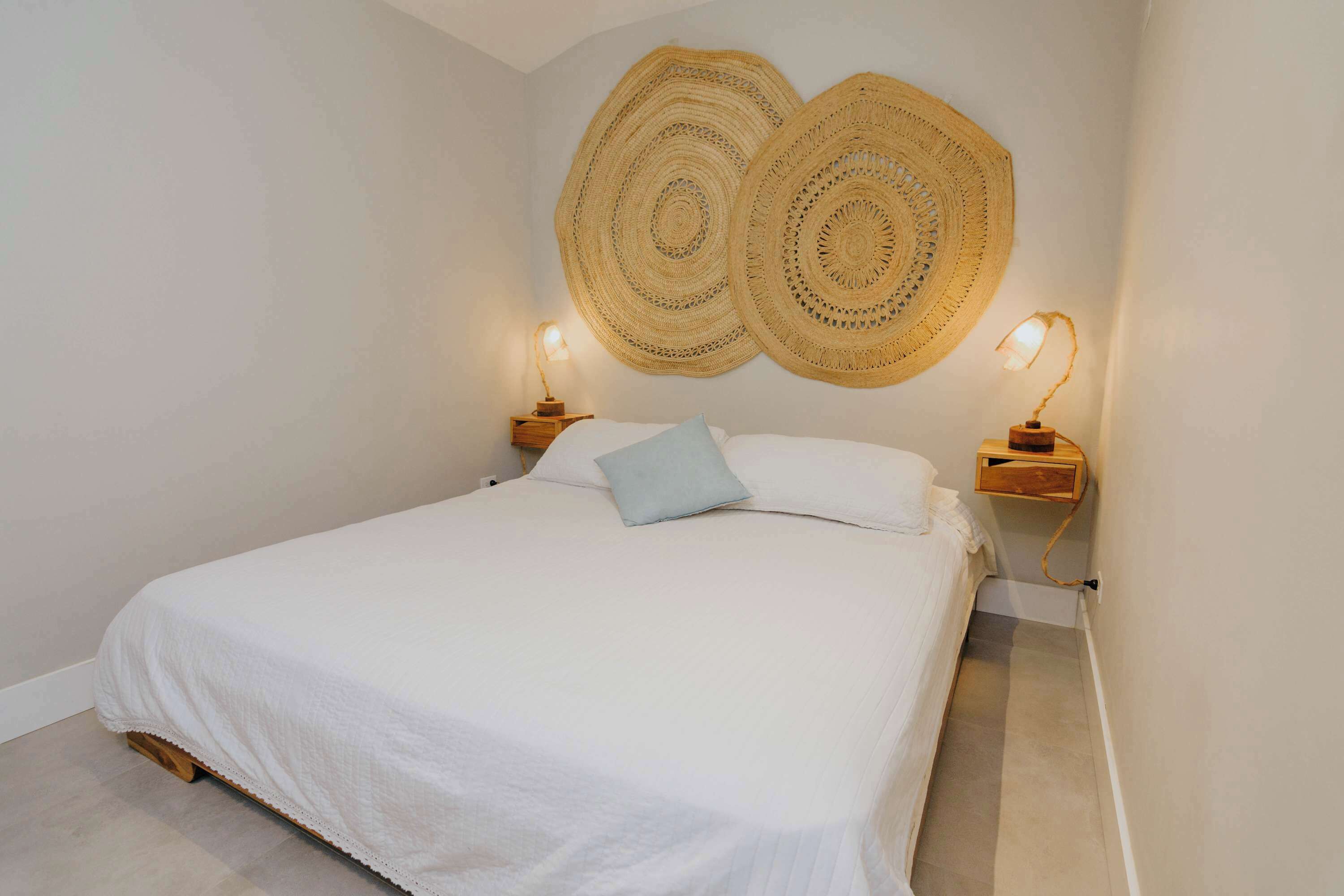 A bedroom with a large bed, two bedside lamps, and two wall-mounted woven wall hangings.