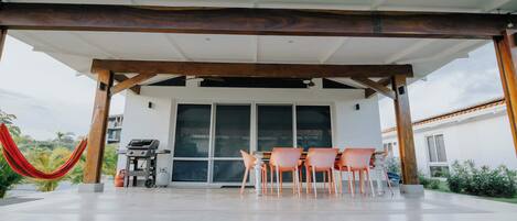 A covered outdoor patio with a grill, chairs, and a hammock.