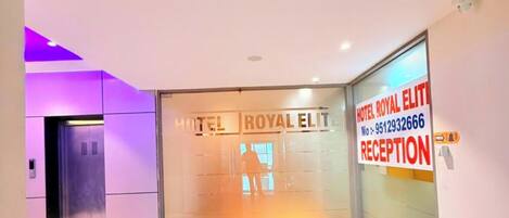 A reception area with a reception desk, a glass wall, and a sign for Hotel Royal Elite.