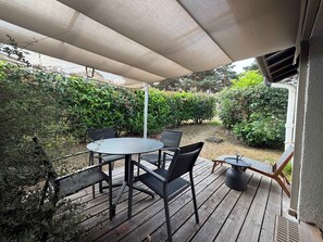 A covered outdoor seating area with a table and chairs, surrounded by greenery. - T2 appartement 1 chambre en RDJ avec terrasse (Anglet)