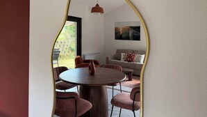 A dining area with a round table and chairs, a sofa, and a painting on the wall. - T2 appartement 1 chambre en RDJ avec terrasse (Anglet)