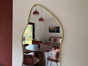 A dining area with a round table and chairs, a sofa, and a painting on the wall. - T2 appartement 1 chambre en RDJ avec terrasse (Anglet)