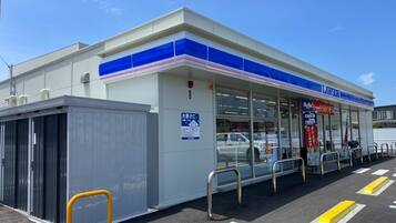 A Lawson convenience store with a clear entrance, a parking lot with marked spaces, and a small enclosed area to the left.