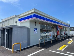 Een Lawson gemakswinkel met een duidelijke ingang, een parkeerplaats met aangegeven plekken, en een klein afgesloten gedeelte aan de linkerkant.