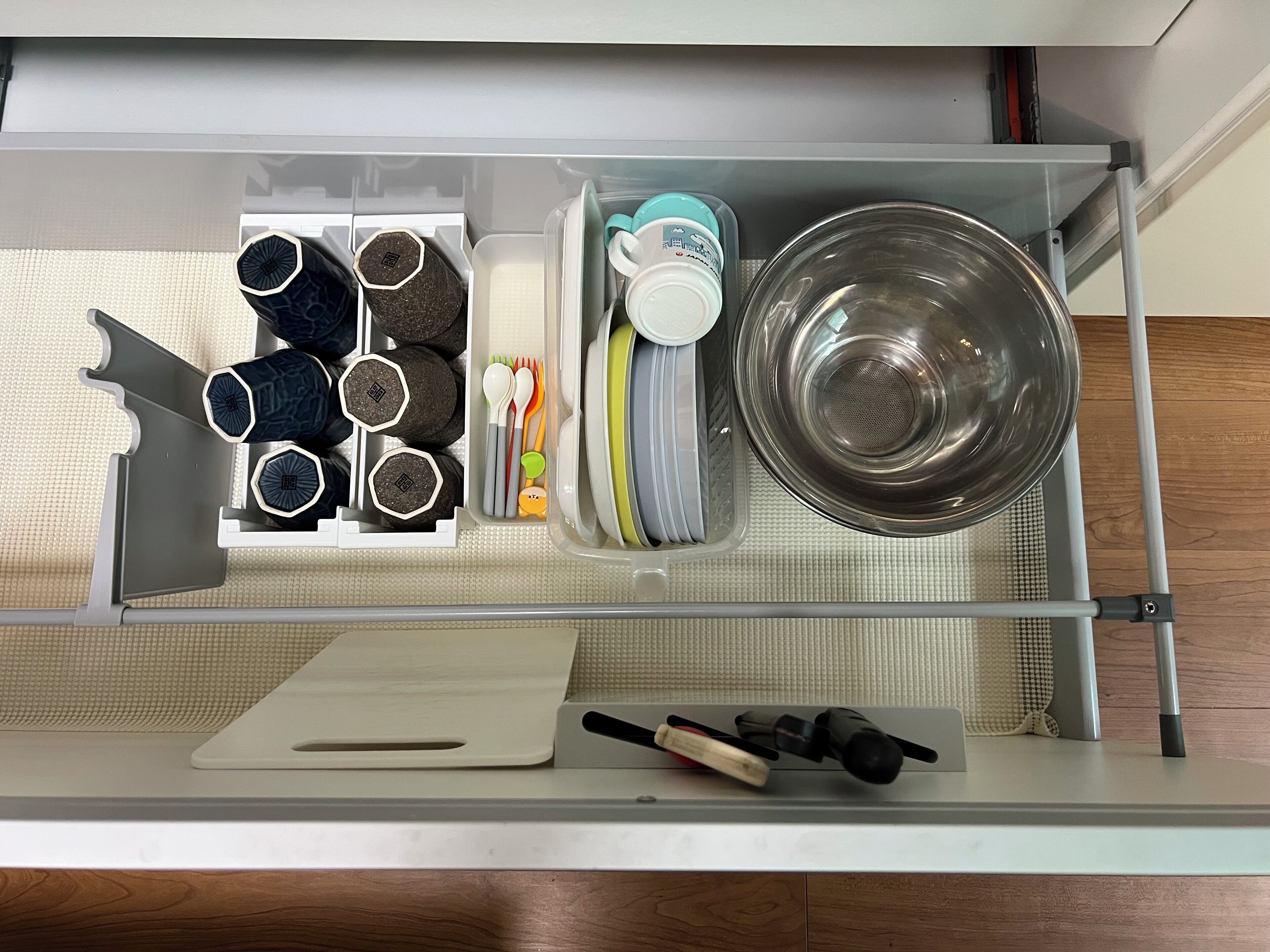 A kitchen drawer with utensils, a cutting board, and a metal bowl.