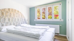 Ein Schlafzimmer mit einem Bett, einem Heizkörper und einem Fenster mit Blick auf Bäume.