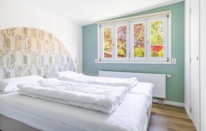 Ein Schlafzimmer mit einem Bett, einem Heizkörper und einem Fenster mit Blick auf Bäume.