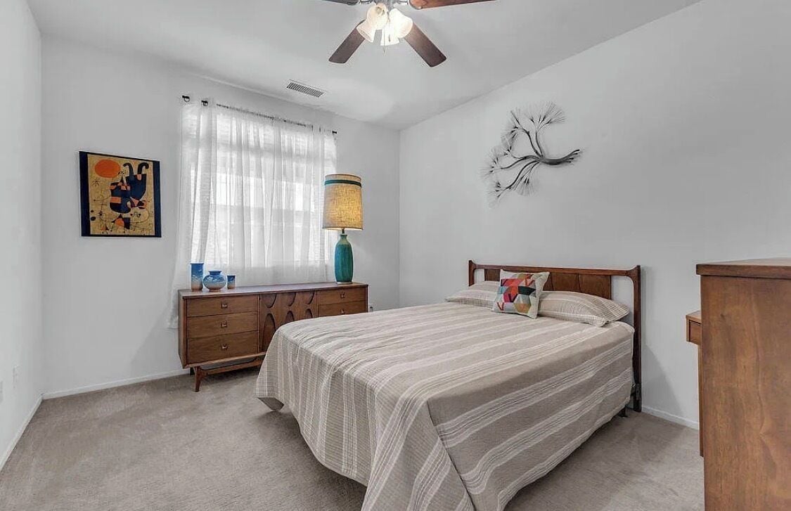 Ein Schlafzimmer mit Bett, Kommode, Lampe, Deckenventilator und einem Wandbild.
