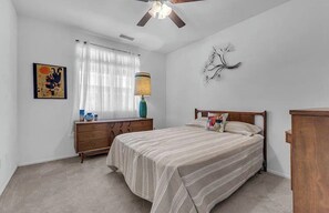 Ein Schlafzimmer mit Bett, Kommode, Lampe, Deckenventilator und einem Wandbild.