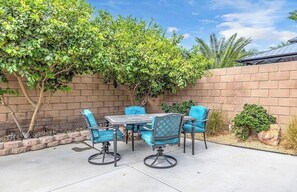 Un patio al aire libre con pared de ladrillo, una mesa con sillas y un árbol que da sombra.