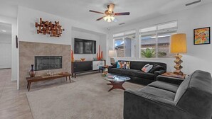 Ein modernes Wohnzimmer mit Kamin, Deckenventilator, einer Couch, einem Couchtisch und einem Fernseher.