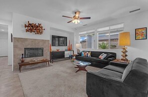 Ein modernes Wohnzimmer mit Kamin, Deckenventilator, einer Couch, einem Couchtisch und einem Fernseher.