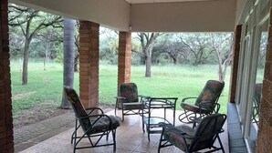 A covered patio area with tiled flooring, outdoor furniture, and a view of a grassy landscape.