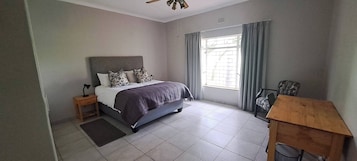 Un dormitorio con cama, escritorio, silla, ventana con cortinas y ventilador de techo.