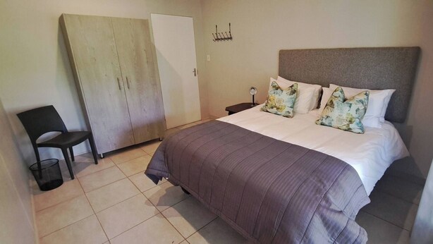 A bedroom with a bed, a chair, a wardrobe, and a wall-mounted light fixture.