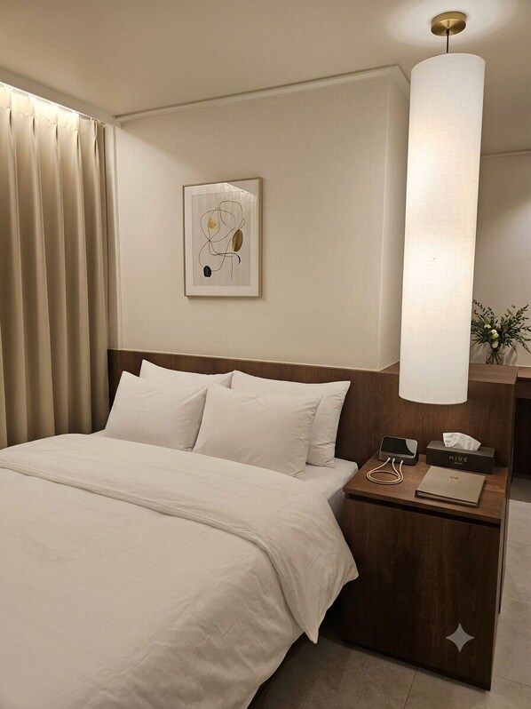 A hotel room with a bed, bedside table, lamp, and artwork on the wall.
