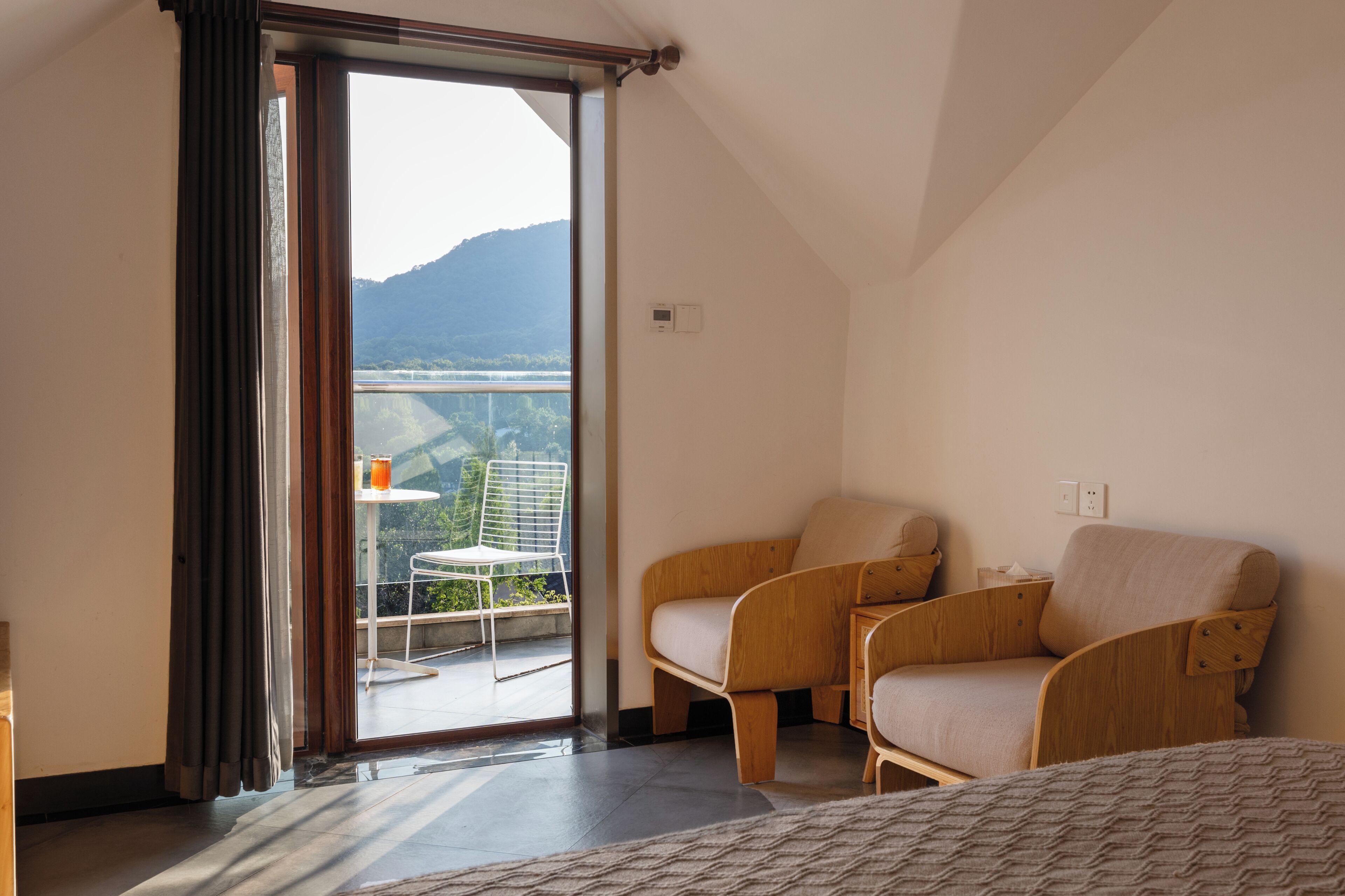 A hotel room with a balcony, two wooden chairs, a small table, and a bed.