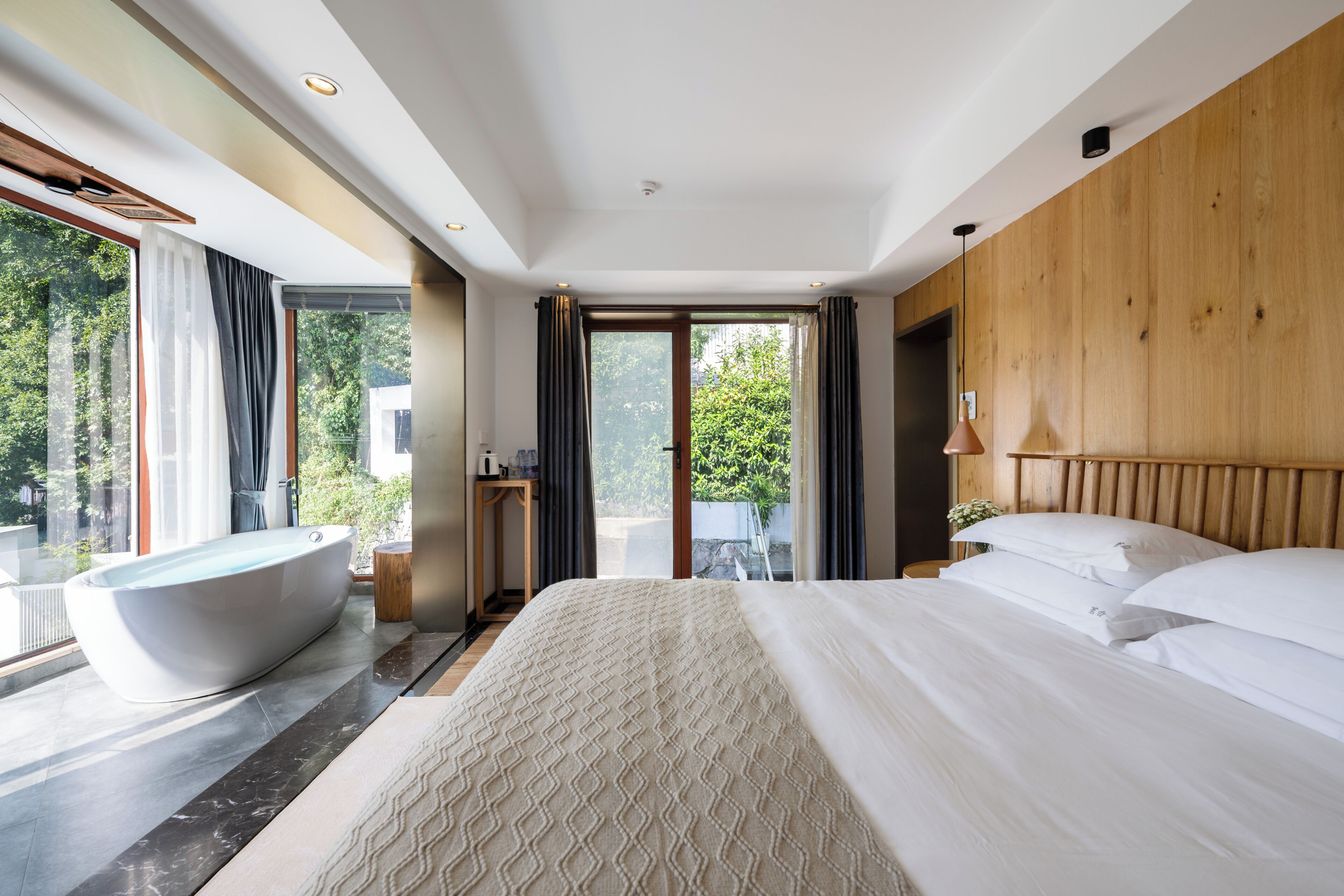 Quarto de hotel moderno com uma cama grande, uma banheira e vista para o verde.