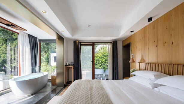 Een moderne hotelkamer met een groot bed, een badkuip en uitzicht op groen.