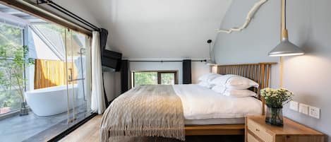 Un dormitorio moderno con una cama grande, una mesita de noche de madera, una lámpara colgante y vistas al exterior.