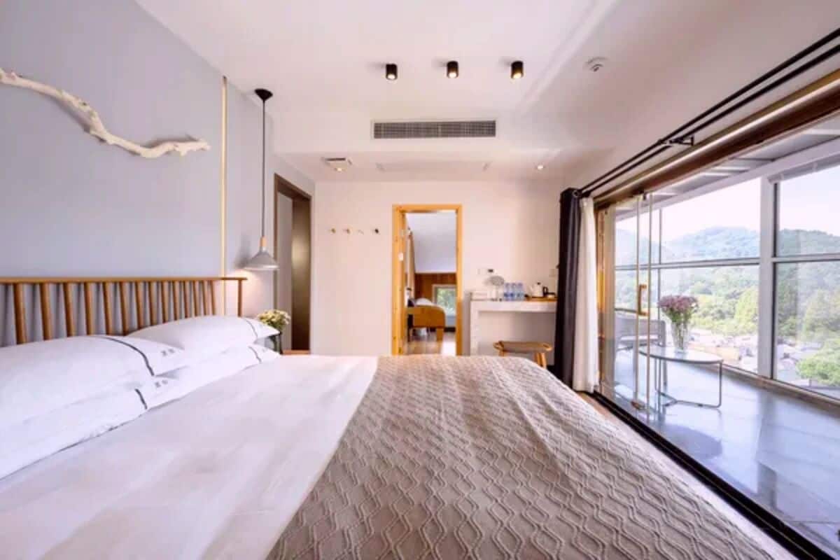 A hotel room with a large bed, a view of the outdoors, and a bathroom with a mirror and sink.