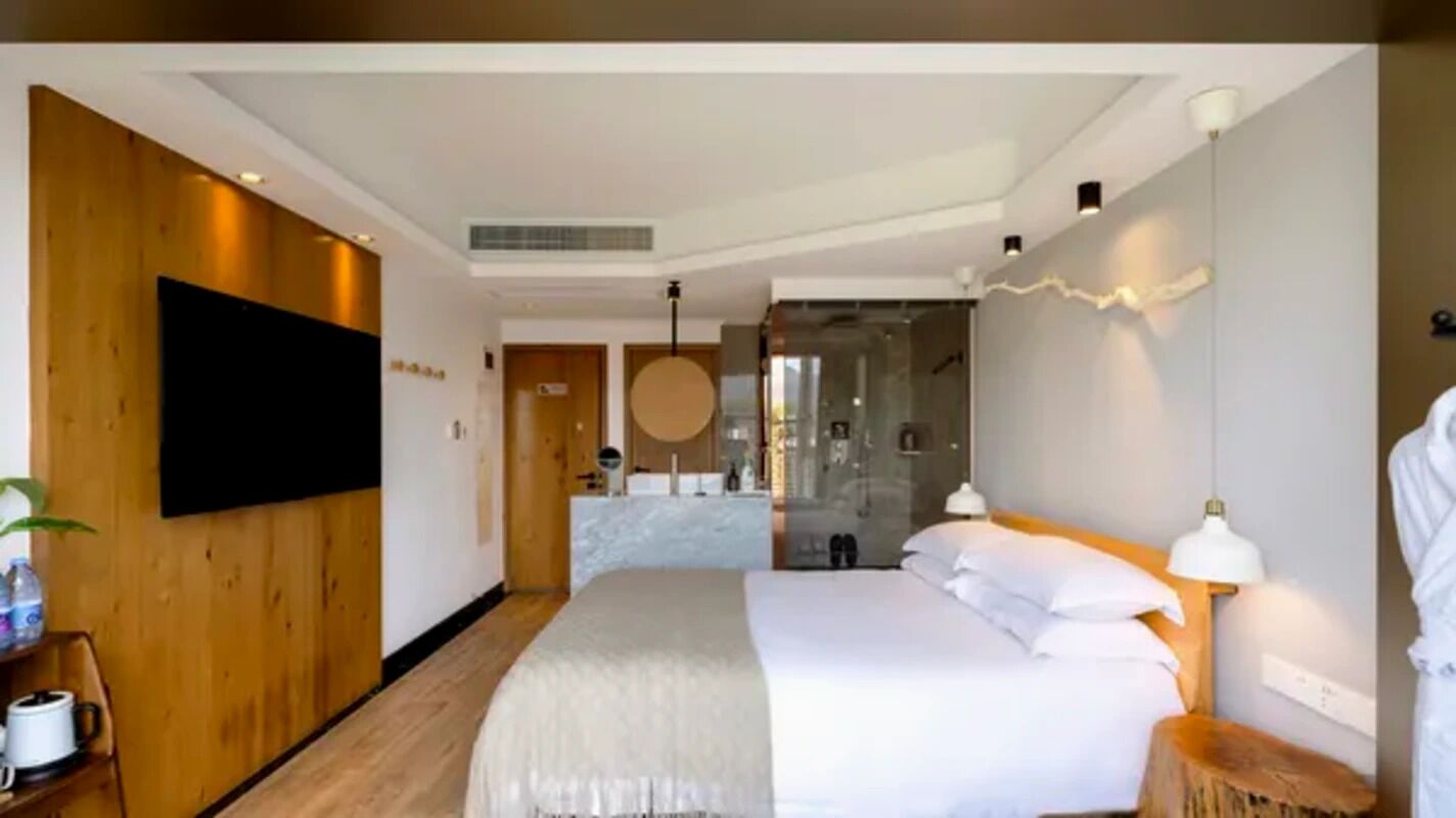 Ein modernes Hotelzimmer mit einem großen Bett, einem flachbildschirmfernseher an der Wand, einer Holzvertäfelung und einem durchgehenden Türspalt einsehbarer Badezimmer.