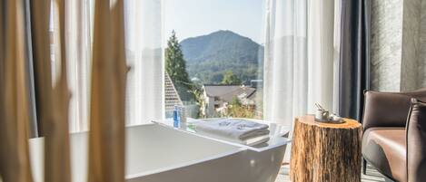 A modern bathroom with a freestanding bathtub, a wooden side table, and a leather chair.