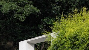 Een wit gebouw met een poort, omringd door begroeiing en een betonnen muur.