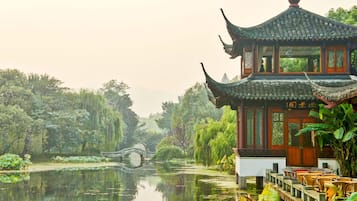 A traditional Chinese pavilion by a tranquil pond with a bridge in the background.