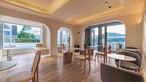 Een modern interieur met houten vloeren, ronde tafels en stoelen, grote ramen met uitzicht op groen en heuvels.
