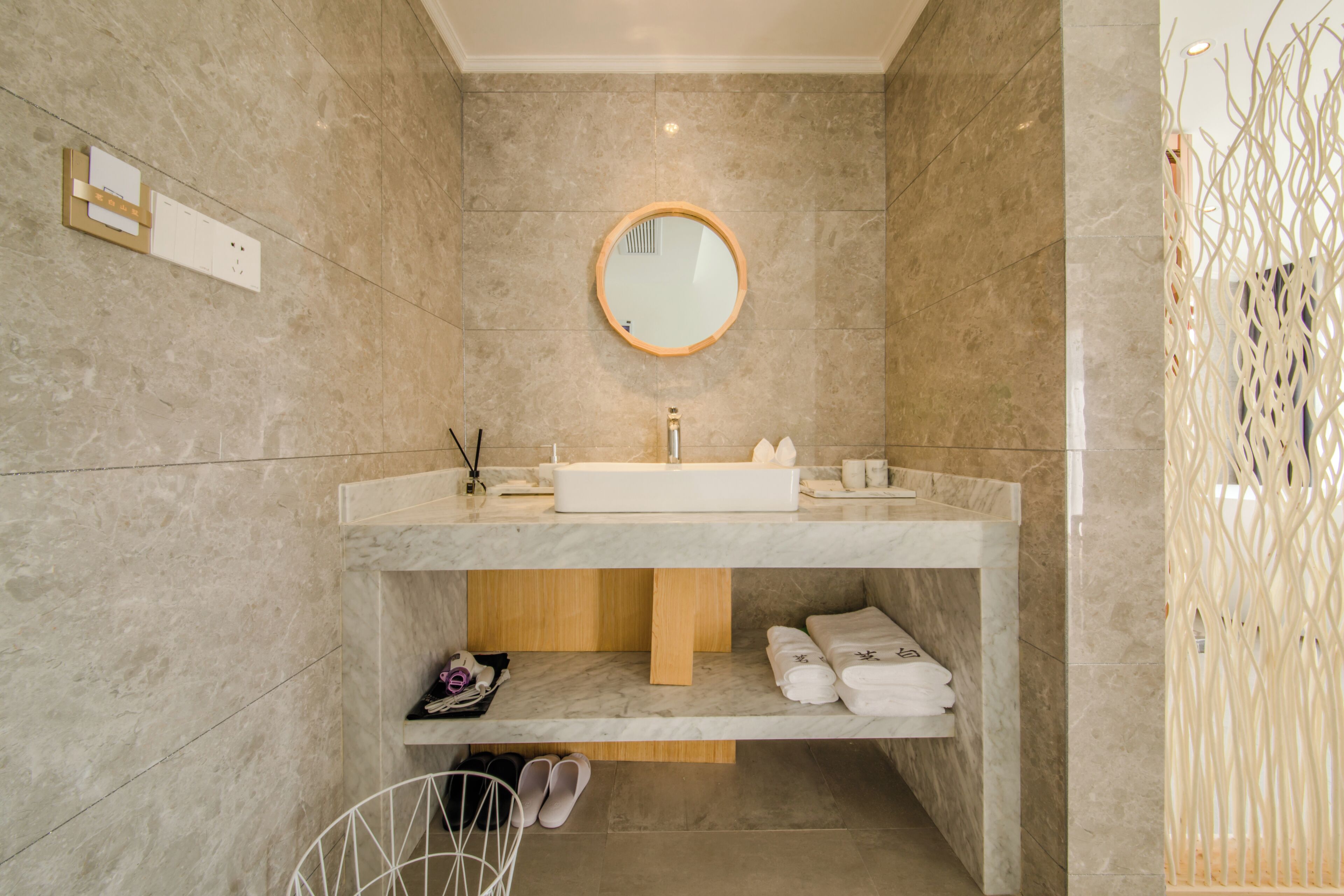 Une salle de bain moderne avec un sol en marbre, un lavabo intégré, un miroir et une étagère avec des serviettes.