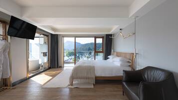 A hotel room with a bed, a TV, a sofa, and a view of a mountainous landscape.