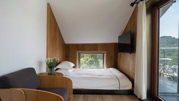 Een slaapkamer met een bed, een aan de muur bevestigde televisie, een raam met uitzicht op groen en een houten vloer.