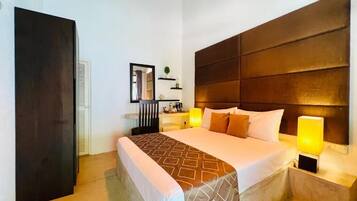 Habitación de hotel con una cama grande, lámparas de noche, cabecera oscura y una mesita de noche pequeña.
