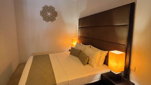 Un dormitorio con cama, lámparas de noche, un adorno en la pared y una alfombra.
